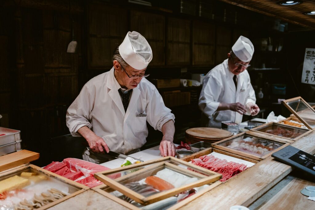 A master sushi chef is skillfully preparing fresh sashimi at a traditional wooden counter, showcasing culinary expertise and the finest ingredients. This scene captures the essence of a sophisticated dining experience often found in fine dining restaurants, where guests can savor exquisite flavors and enjoy impeccable service.