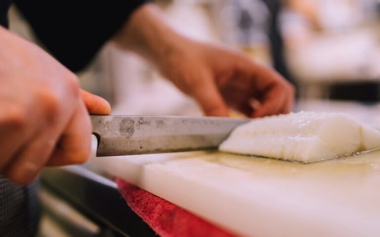 A Japanese chef is meticulously preparing sashimi using traditional knives on a cutting board, showcasing the culinary mastery of Japanese cuisine. The scene highlights the chef's attention to detail, emphasizing the freshness of the ingredients and the artistry involved in creating signature dishes for a fine dining experience.