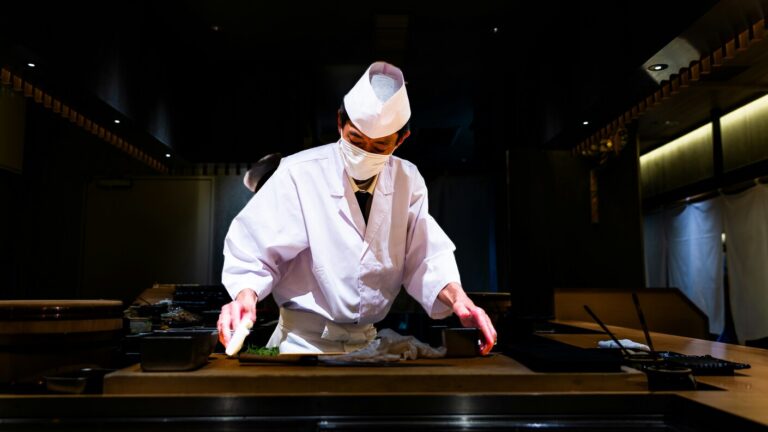 An intimate omakase counter showcases a chef skillfully presenting seasonal dishes to diners, highlighting the artistry of Japanese cuisine. Guests enjoy a refined dining experience with fresh ingredients, including sushi and sashimi, while savoring the culinary mastery of this Japanese restaurant in Singapore.
