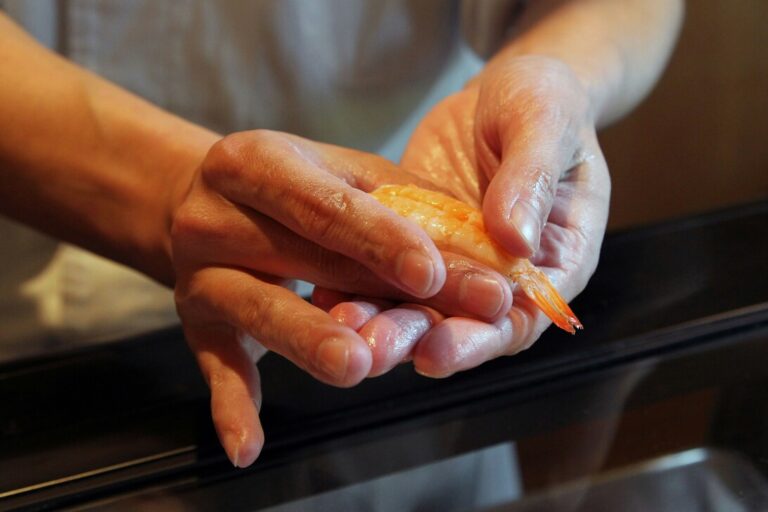 A skilled chef prepares fresh sushi at a traditional counter, showcasing seasonal ingredients like fish and vegetables in a vibrant display. This scene captures the essence of Japanese cuisine and dining, highlighting the artistry and culinary techniques involved in creating signature dishes.