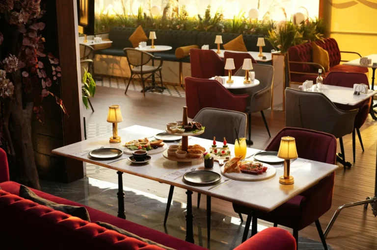 Elegant restaurant interior with a marble table set for four. It’s adorned with diverse dishes, warm ambient lighting, and surrounded by plush red and gray chairs.