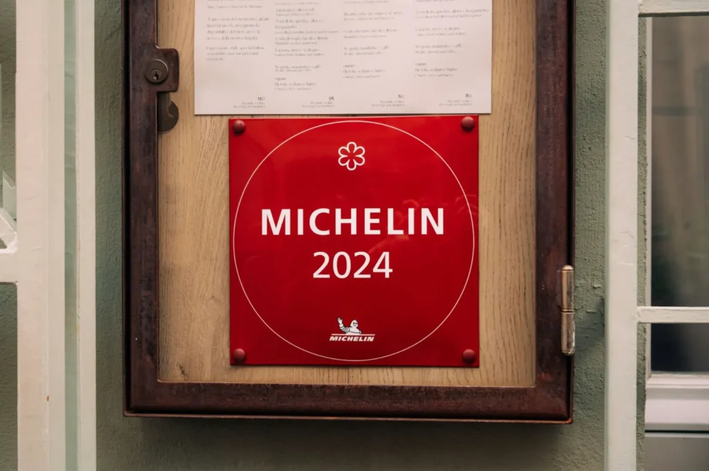 Red "Michelin 2024" plaque with a star symbol, displayed on a wooden frame beneath a menu. The setting conveys prestige and recognition.