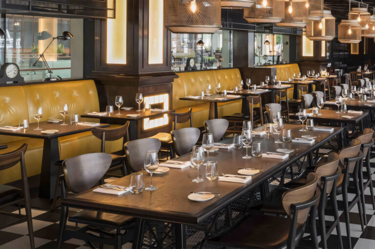 The stylish dining room of Bread Street Kitchen, featuring yellow leather banquettes, dark wood tables, and a black and white checkered floor.