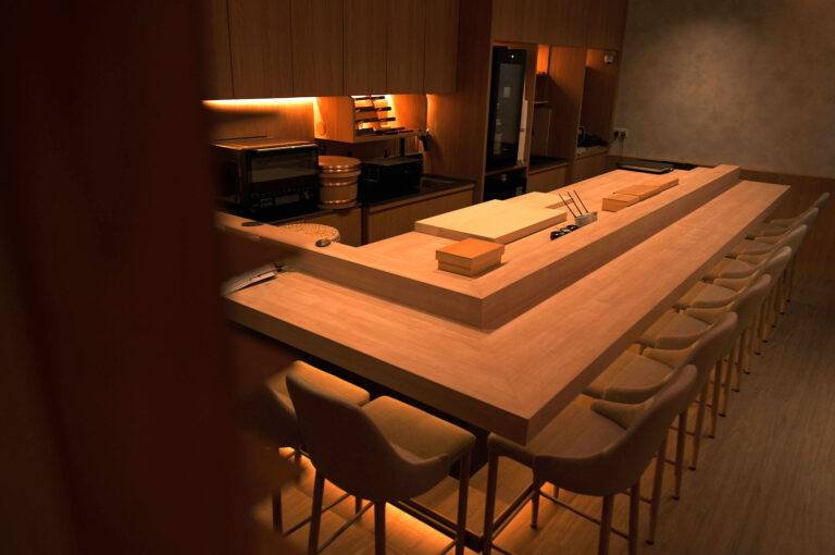 Elegant, minimalist wooden omakase sushi counter with seating for guests and warm lighting.