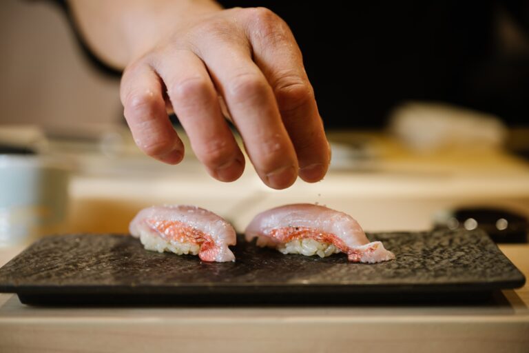 A chef lightly sprinkling salt over a freshly prepared piece of sushi for added flavour and refinement