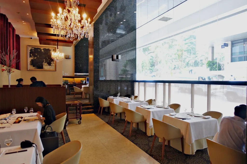 An elegant restaurant dining room with tables set for meals and large windows overlooking an outdoor scene.