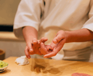 Singapore Best Food : A Japanese chef is meticulously preparing sushi, showcasing his culinary skills against the backdrop of Singapore's Marina Bay skyline visible through the restaurant windows. The scene captures the essence of fine dining, blending traditional Japanese artistry with the vibrant atmosphere of Singapore's best food culture.
