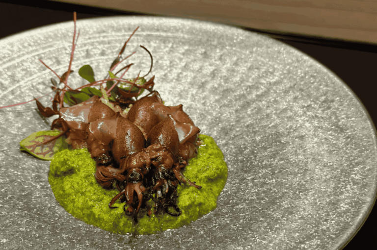 Artfully plated firefly squid on a vibrant green spring puree, garnished with microgreens and served on a textured glass dish. A refined celebration of shun, capturing the fleeting brilliance of seasonal seafood in Japanese cuisine.