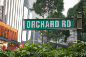 Street sign for Orchard Road in Singapore, framed by lush greenery and glowing high-rise buildings at dusk; sets the scene for a culinary journey through the district’s seasonal sushi offerings.