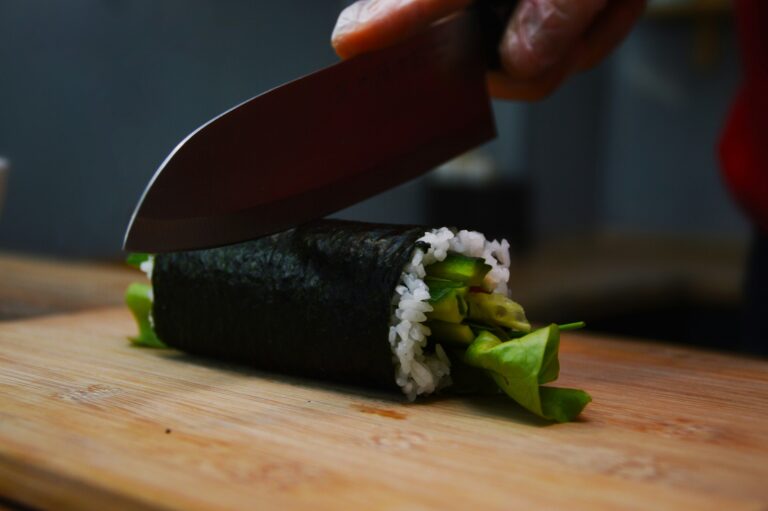 Modern sushi rolls filled with imitation crab, avocado, and cucumber being precisely sliced by a skilled chef