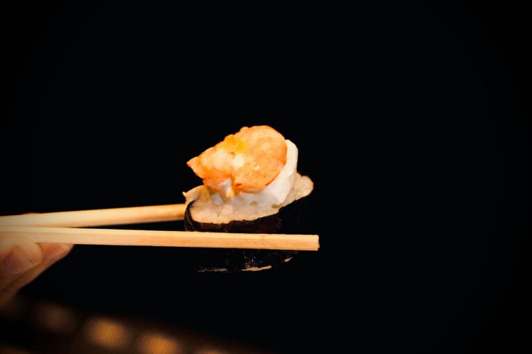 Best food in SG : A close-up shot of chopsticks holding a delicate piece of sushi, highlighting the precision and artistry of Japanese cuisine.