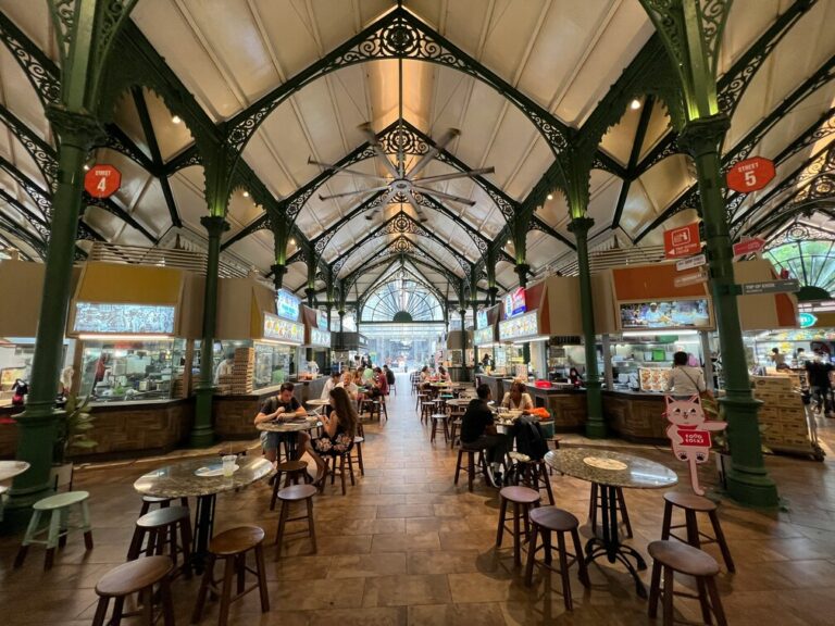 A bustling hawker center filled with various food stalls serving a wide array of delicious dishes, including Hainanese chicken rice and fried chicken. Diners enjoy their meals at communal tables, surrounded by the enticing aromas of traditional Singaporean food like bak kut teh and kaya toast.