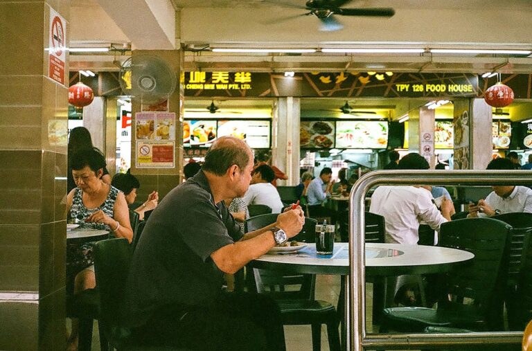 Best food in SG : A man enjoying his meal at a bustling Singapore food court, surrounded by vibrant hawker stalls and local dishes.