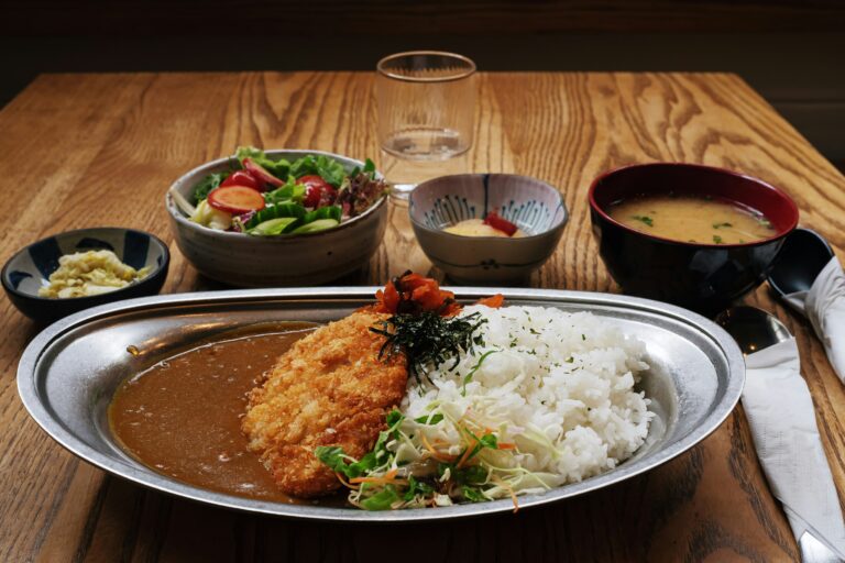 Japanese Food in SG : A hearty plate of Japanese curry served with crispy side dishes on a wooden table, showcasing the comforting flavours of Japan in Singapore’s casual dining scene.