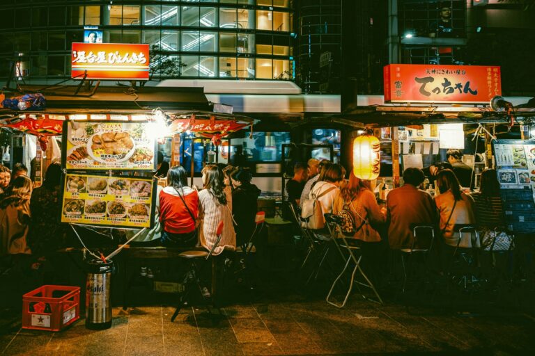 Japanese Food in SG : A vibrant Singapore street lined with food stalls serving Japanese favourites like takoyaki, yakitori, and ramen under softly glowing lanterns.