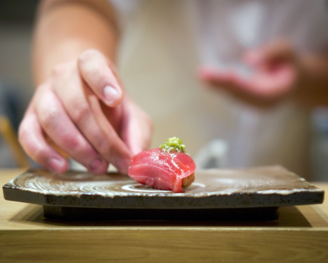 Sashimi Restaurant: A master chef skillfully prepares fresh sashimi at a traditional counter, showcasing precision with his knives as he slices salmon and other fish. The ambiance of the sashimi restaurant reflects a blend of Japanese tradition and modern dining, inviting guests to indulge in this exquisite dish.