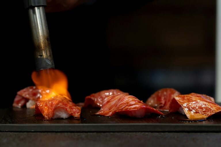 Chef lightly torching the top layer of sushi, creating a smoky aroma and caramelised finish