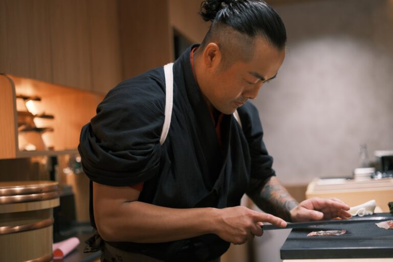 Chef Masa skillfully slicing fresh fish at the sushi counter, demonstrating refined knife techniques and dedication to quality ingredients