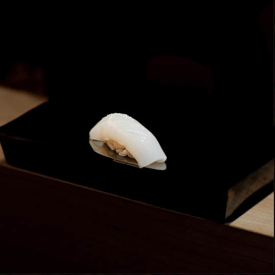 A beautifully arranged piece of fresh sushi, highlighting its clean cut, glossy texture, and impeccable craftsmanship.