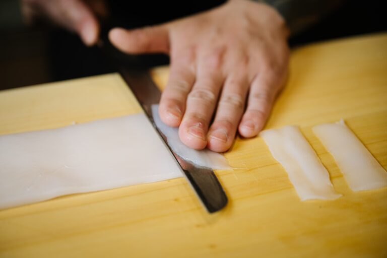 A Japanese chef skillfully slicing fresh fish on a wooden board, showcasing precise knife work and traditional omakase preparation techniques