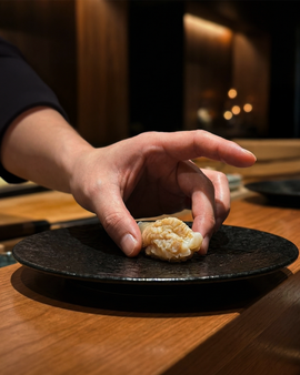 A steady hand carefully sets the sushi onto the plate, completing the dish with quiet elegance and mindful attention to detail.