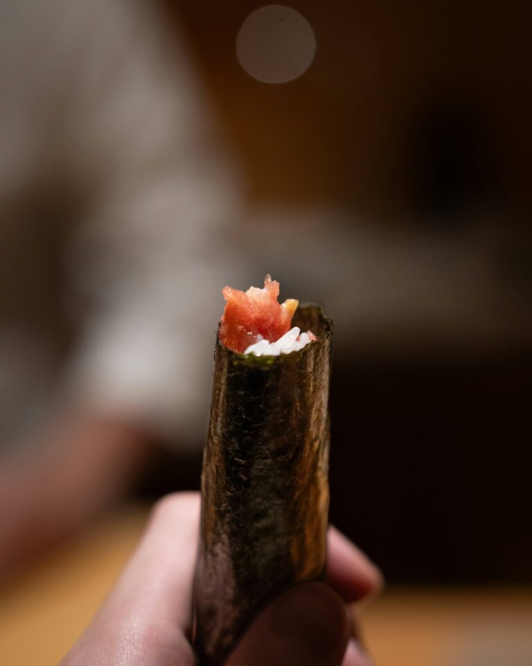 A hand gently holding a mini sushi roll, showcasing its delicate seaweed wrap and fresh, colourful filling.”