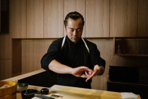 Chef Masa meticulously preparing an omakase dish at the sushi counter, showcasing his precision and years of Japanese culinary mastery.