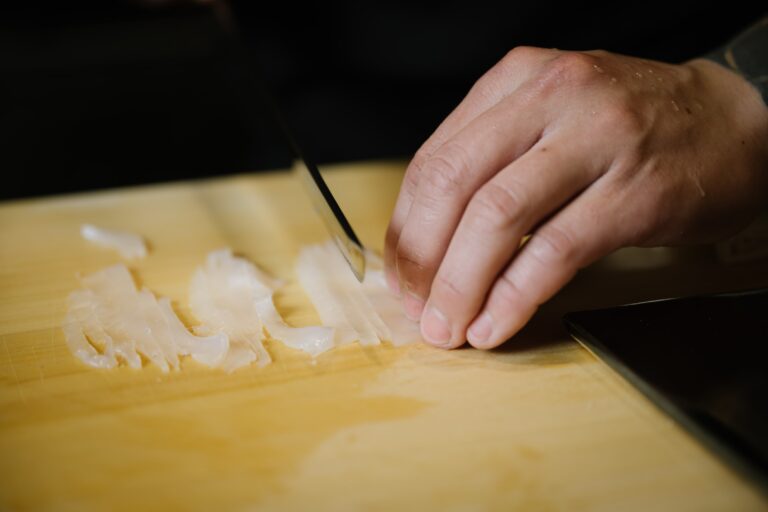 A close-up shot of precise knife work as the chef slices fresh fish with expert control, highlighting the craftsmanship, sharp tools, and refined technique essential in traditional sushi preparation.