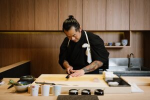 Chef Masa stands at the sushi counter, carefully shaping fresh sushi with precise, refined movements, capturing the artistry of traditional omakase.