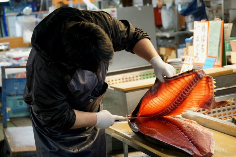 A fishmonger expertly slicing a large tuna at Tokyo’s Toyosu Market, capturing the precision, speed, and intensity of Japan’s famous seafood auctions