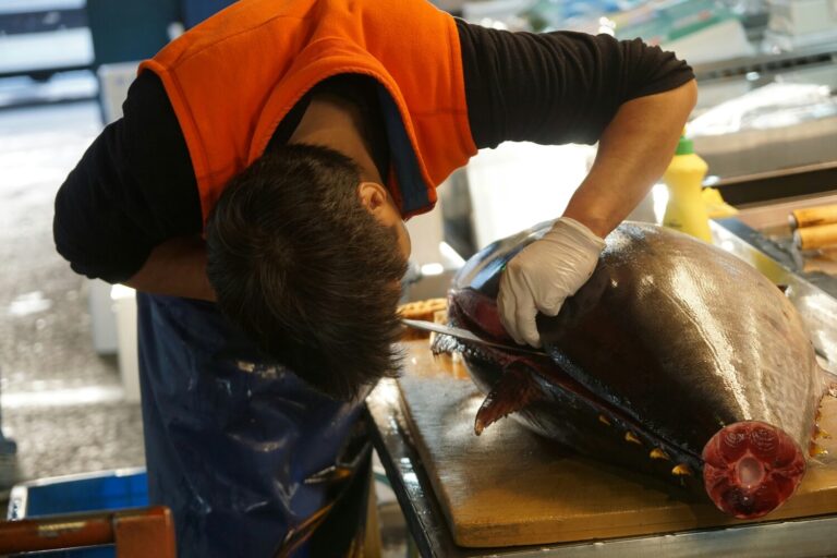 A Japanese fishmonger expertly cutting a large block of tuna at a bustling fish market, preparing premium cuts destined for high-end omakase restaurants in Singapore.