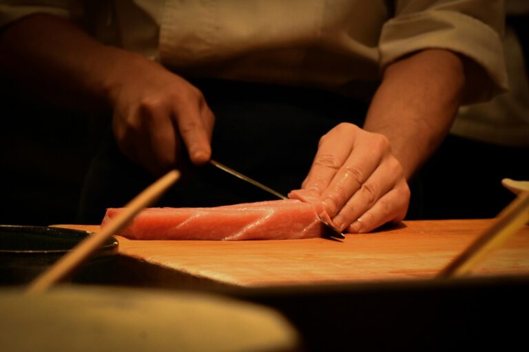 A Japanese chef skillfully slicing fresh fish on a wooden board, showcasing precise knife work and traditional omakase preparation techniques.