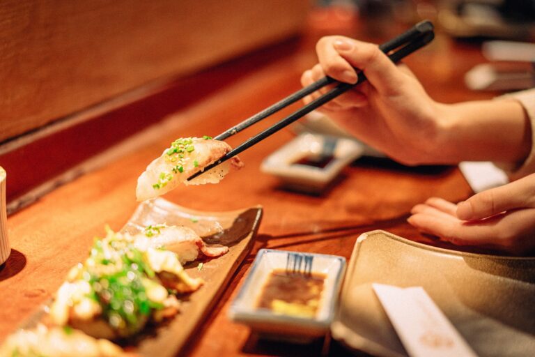 A hand gently lifting a sushi piece with chopsticks, capturing the precision and elegance of enjoying Japanese cuisine.
