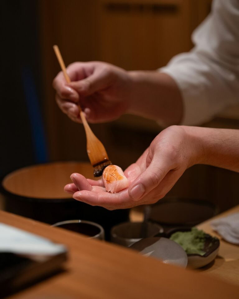 A skilled omakase chef lightly brushing a glaze over freshly prepared sushi, showcasing precision, craftsmanship, and the beauty of traditional Japanese technique.
