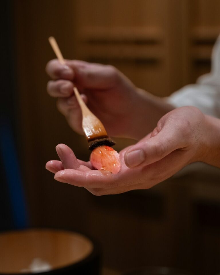 Close-up shot of a chef applying a delicate glaze to freshly prepared sushi, showcasing precision, balance, and classic omakase craftsmanship.