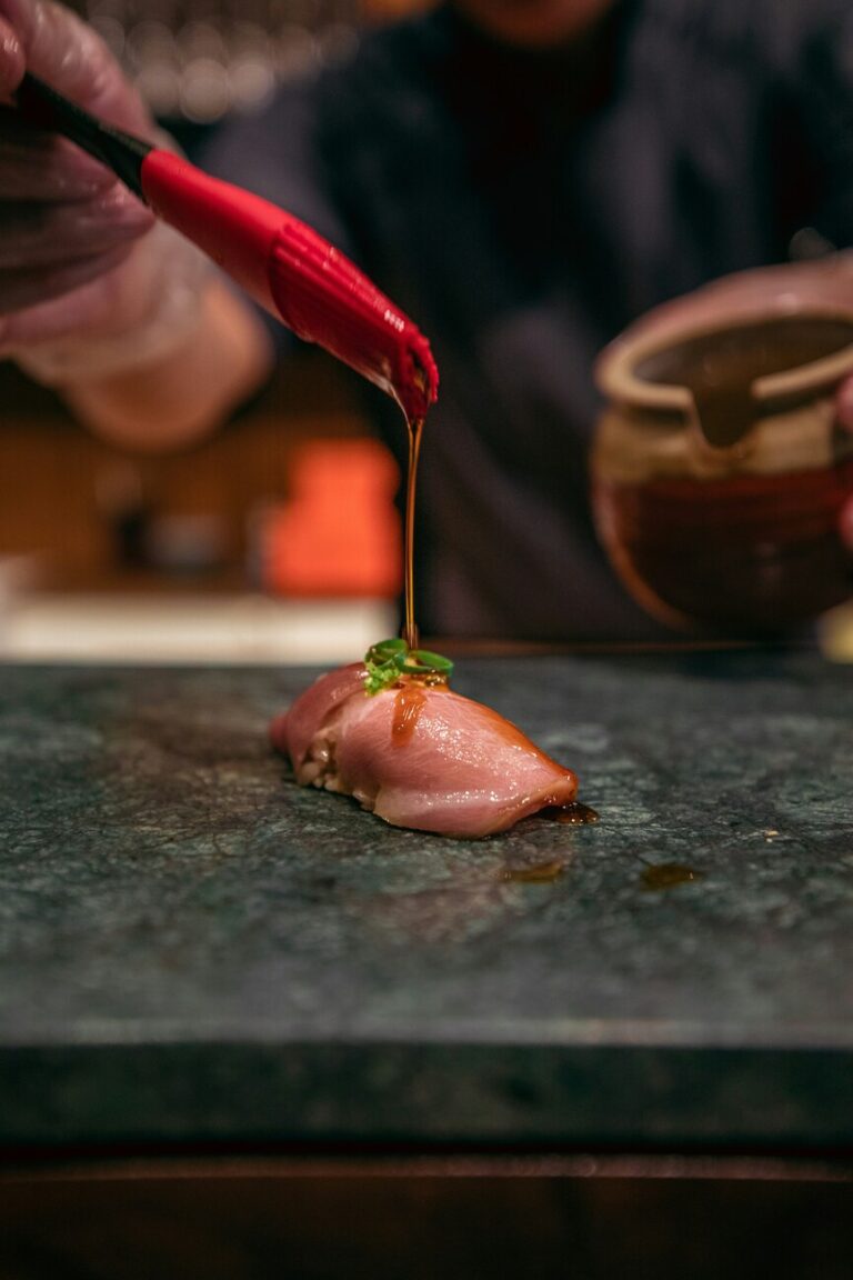 A sushi chef gently brushing a glossy layer of nikiri sauce over a piece of sushi, enhancing its flavour and sheen during an intimate omakase experience.
