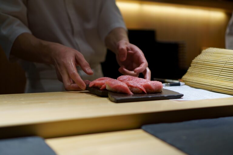 A chef’s hand carefully placing a finished piece of sushi onto the serving board, capturing the grace and attentiveness behind every omakase bite.