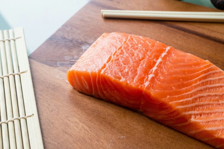 A neatly sliced piece of fresh salmon with rich orange marbling, highlighting its buttery texture and ideal quality for sashimi or sushi.