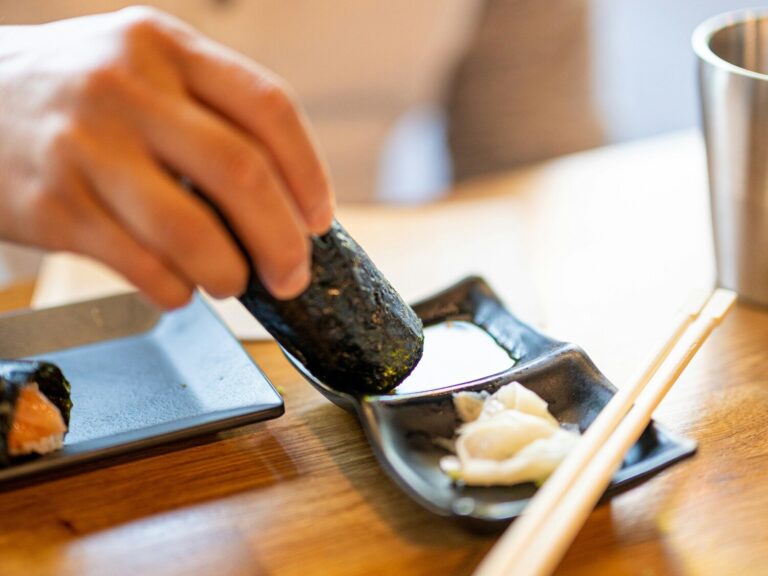 A delicate piece of sushi being gently dipped into a small dish of soy sauce, highlighting the glossy texture of the fish and the refined elegance of Japanese dining.