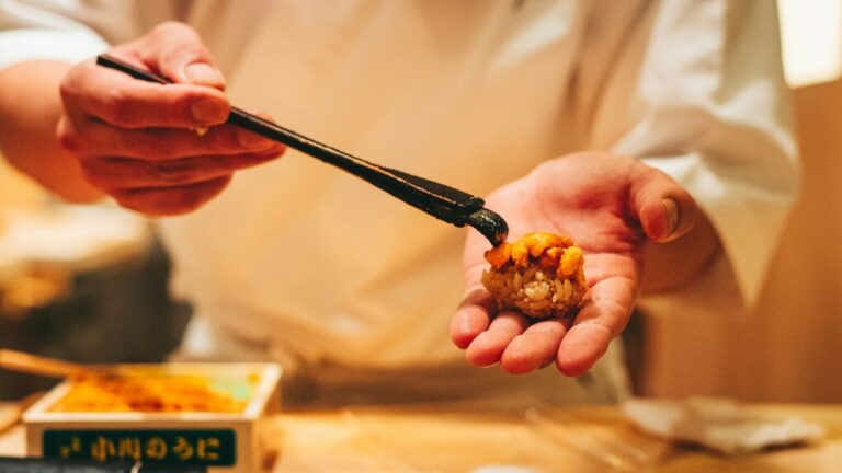A chef carefully brushing a glossy layer of tare sauce over a piece of sushi, adding depth and flavour before serving it to the guest.