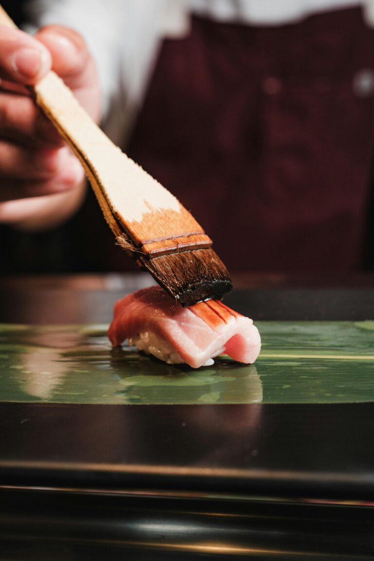 A sushi chef gently brushing a glossy layer of sauce over a piece of sushi during an omakase service, highlighting precision and attention to detail.