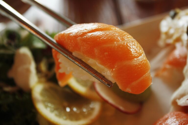 A hand gracefully lifting a sushi piece with chopsticks, showing the texture, freshness, and elegance of the dish up close.