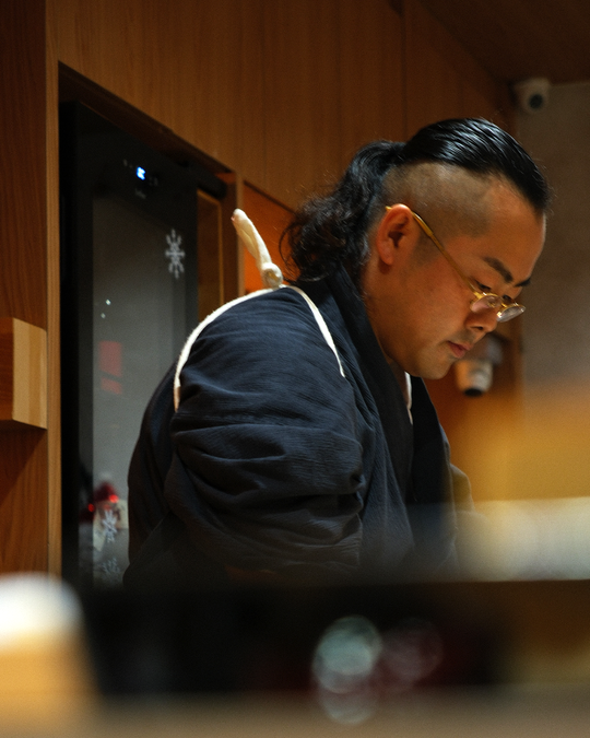 Chef Masa carefully prepares an omakase course behind the counter, his movements calm and precise, reflecting years of discipline and respect for the craft.