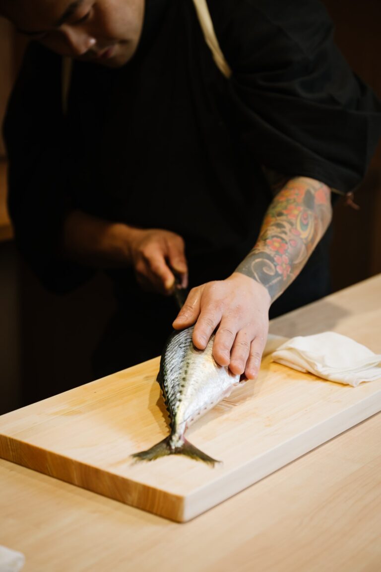 An experienced sushi chef precisely slicing fresh fish with a traditional Japanese knife, reflecting refined knife skills essential to preserving texture, flavour, and presentation in omakase cuisine.