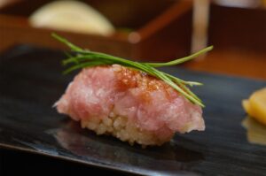 A close-up shot of a Negitoro nigiri sushi topped with fresh green chives, served on a black ceramic plate at a Japanese restaurant.