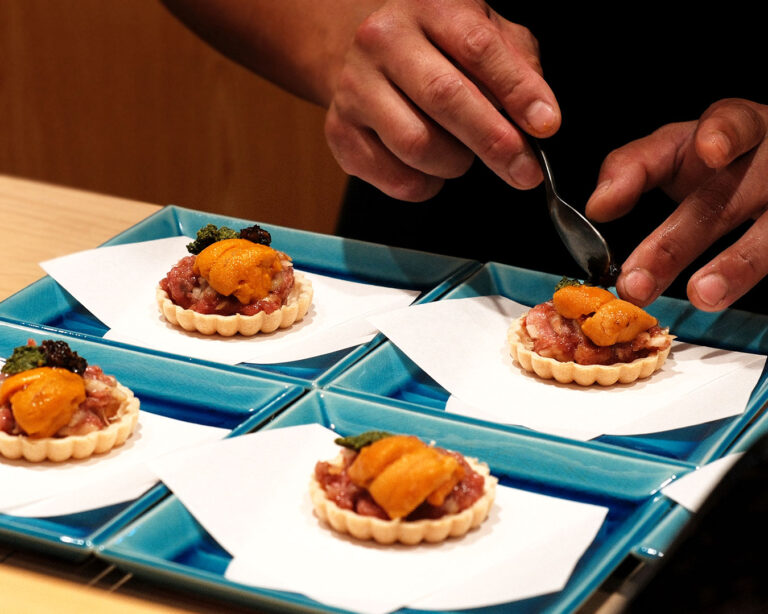 A sushi chef carefully assembles an omakase course, arranging each ingredient with precision and calm focus.