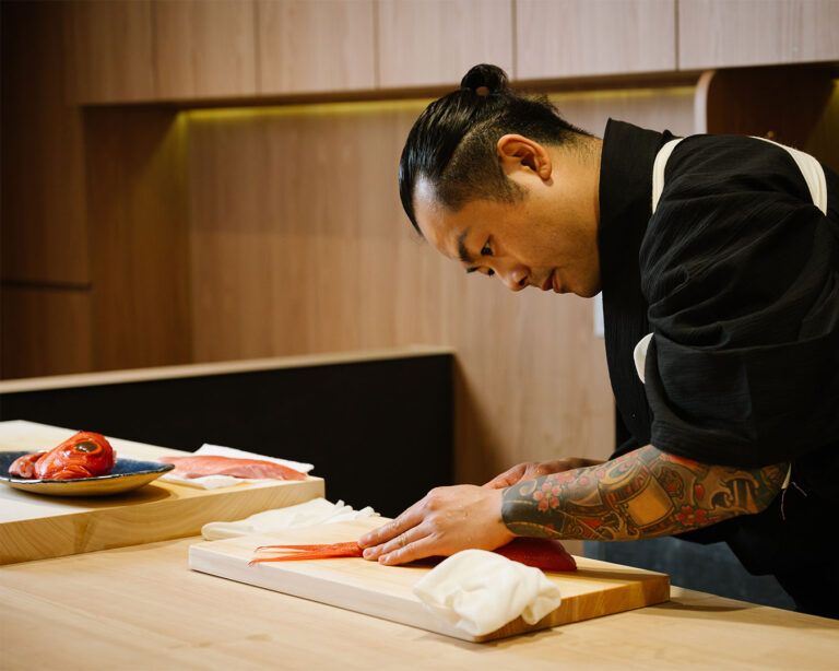 Chef Masa carefully slices a pristine cut of fish with precise movements, showcasing traditional Japanese knife skills at the omakase counter.