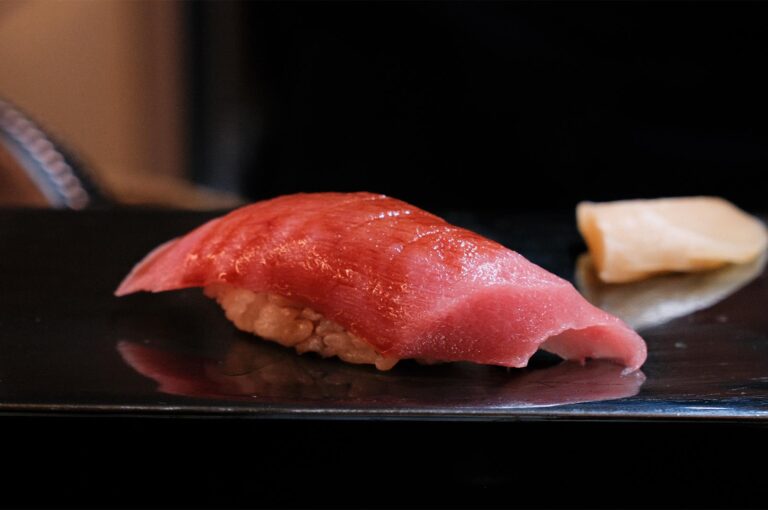 Close-up of a fresh Maguro (tuna) nigiri sushi piece served on a black ceramic plate with a side of pickled ginger.