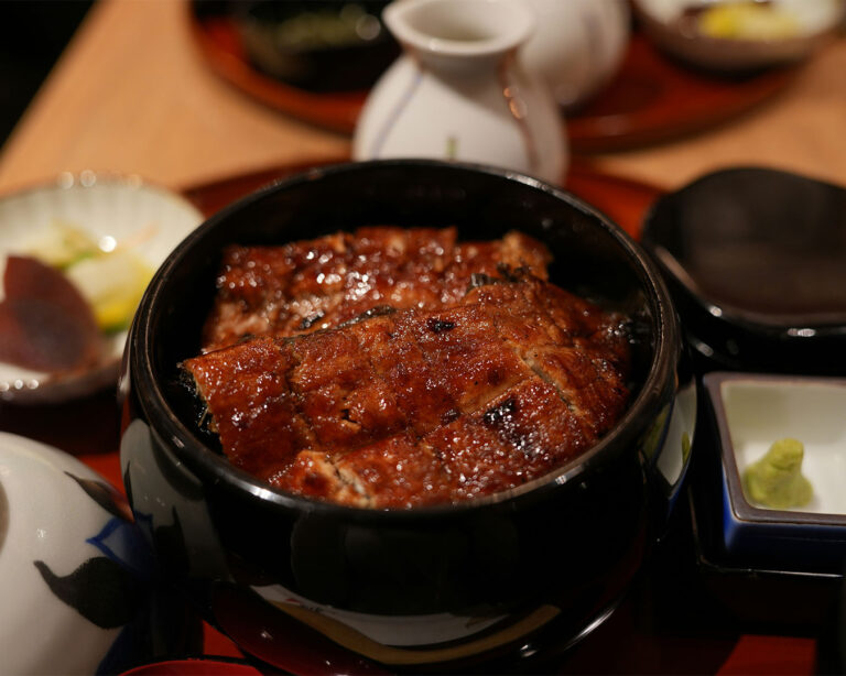 A plated unagi dish with slices of grilled freshwater eel glazed in rich, caramelised sauce, arranged neatly on the plate to showcase its tender meat and signature sweet–savory aroma.