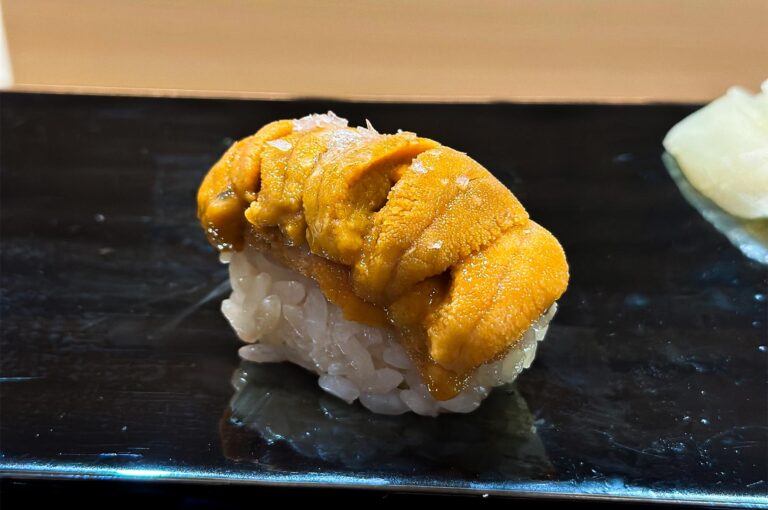 High-quality Uni (sea urchin) nigiri sushi topped with a pinch of sea salt, presented on a sleek black serving tray